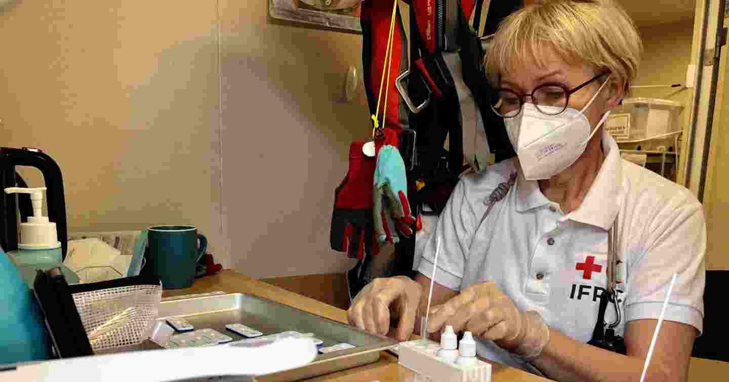 En kvinna med ansiktsmask i halvnärbild som hanterar provrör vid ett skrivbord.