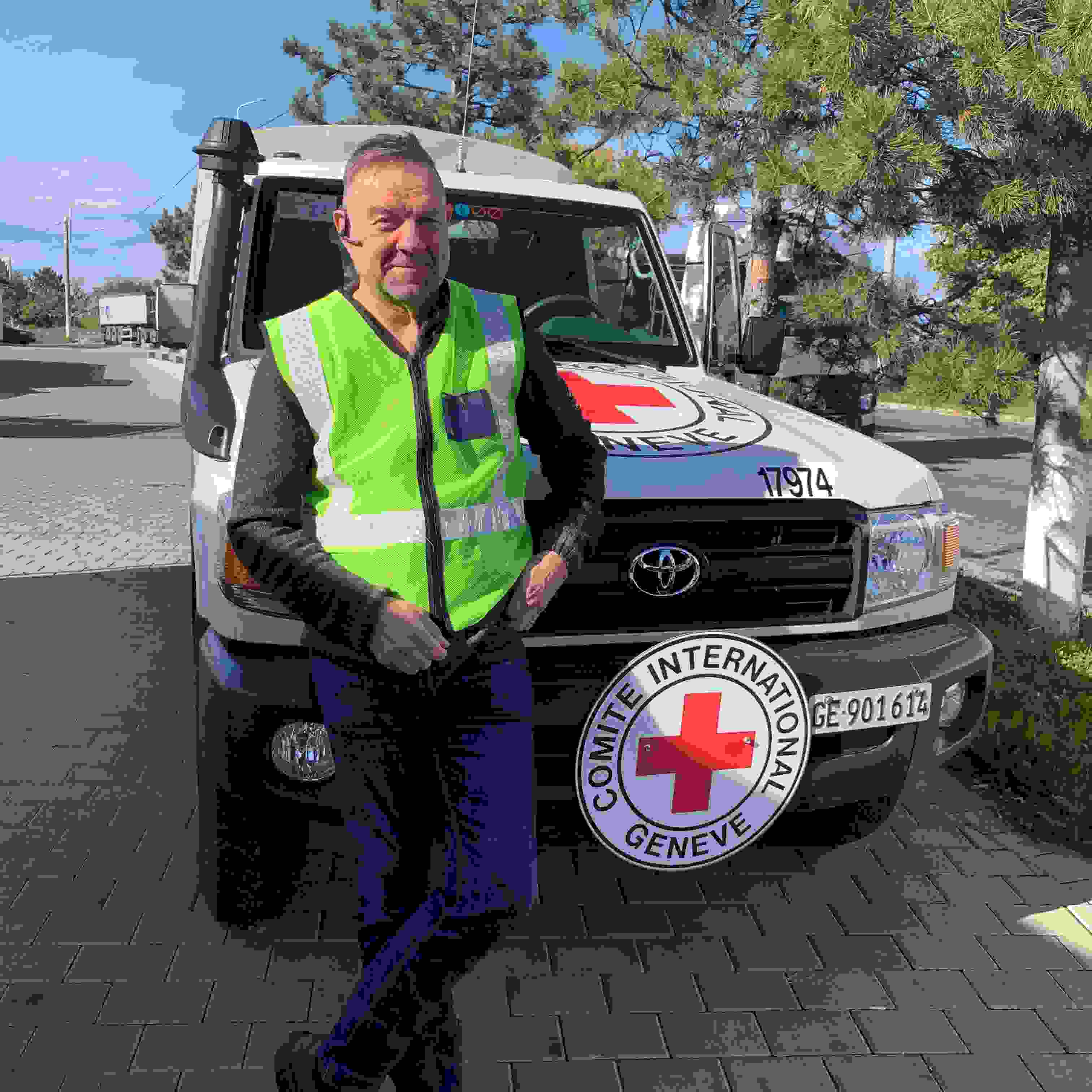 Biståndsarbetare Keijo Eklöf står leende framför internationella Rödakorskommitténs bil.