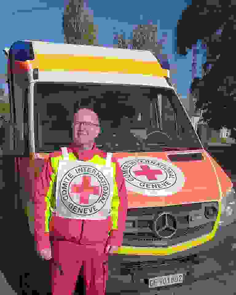 Primärvårdare Tuomo Hämäläinen ler bredvid Röda Korskommitténs ambulans