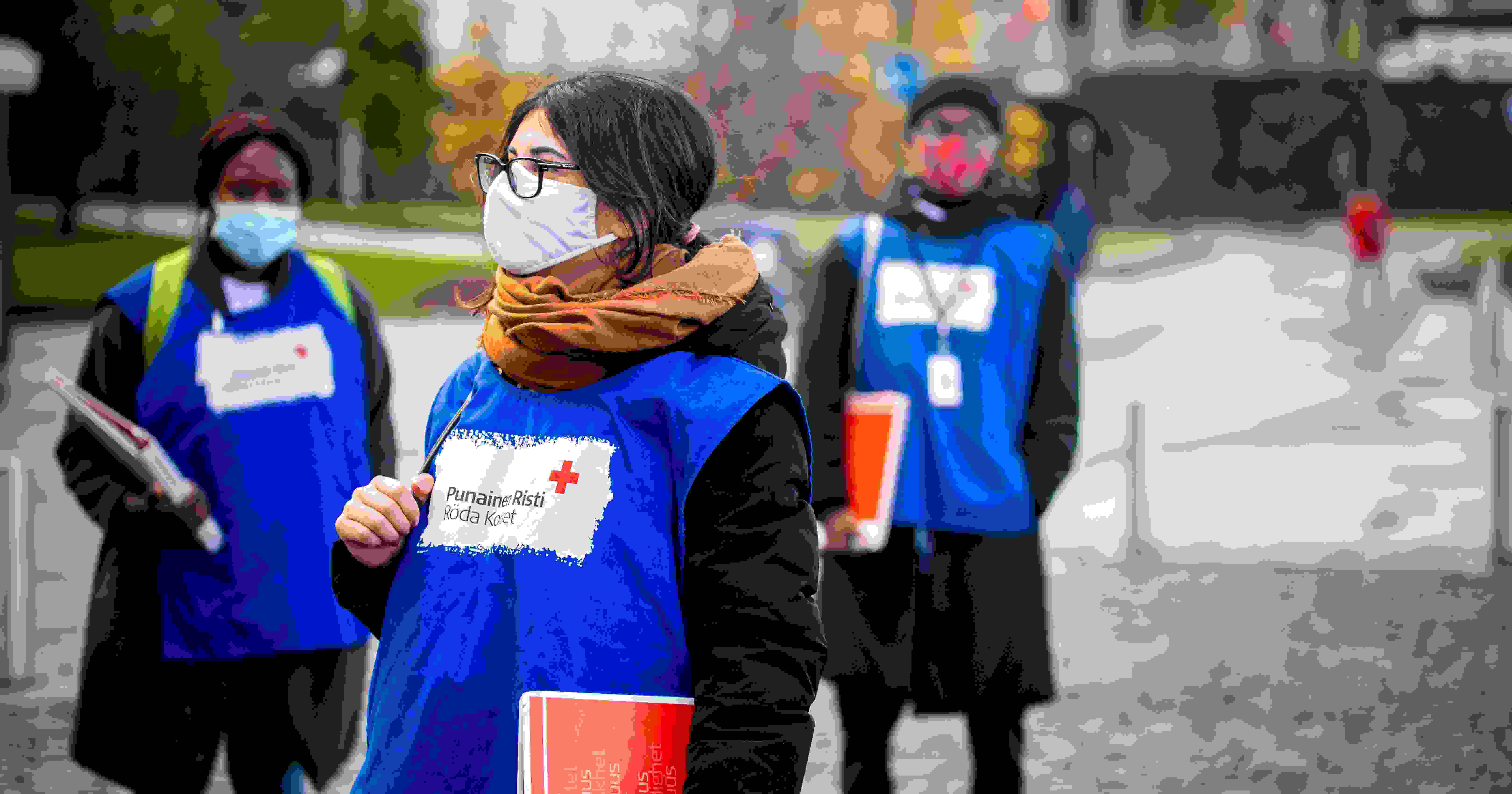 Tre av Röda Korsets face-to-face-insamlare, eller fejssare, står på en gata i Röda Korsets blå västar och med röda mappar i händerna.