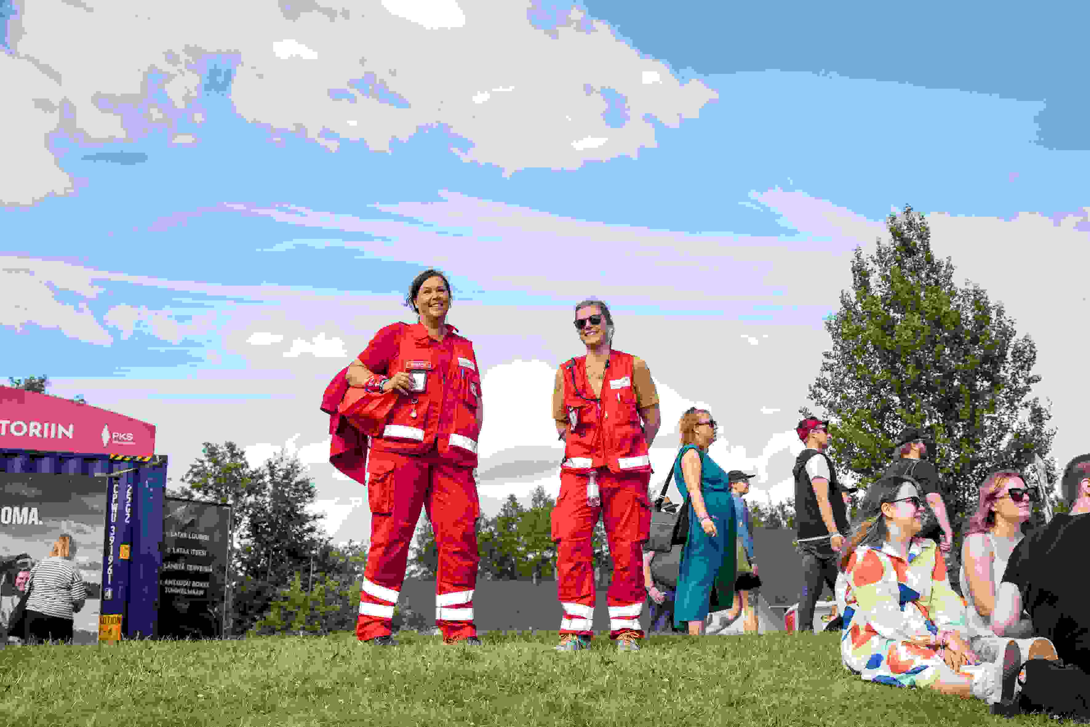 Röda Korsets första hjälpen-jourhavande ler mot kameran i en solig festivalmiljö.