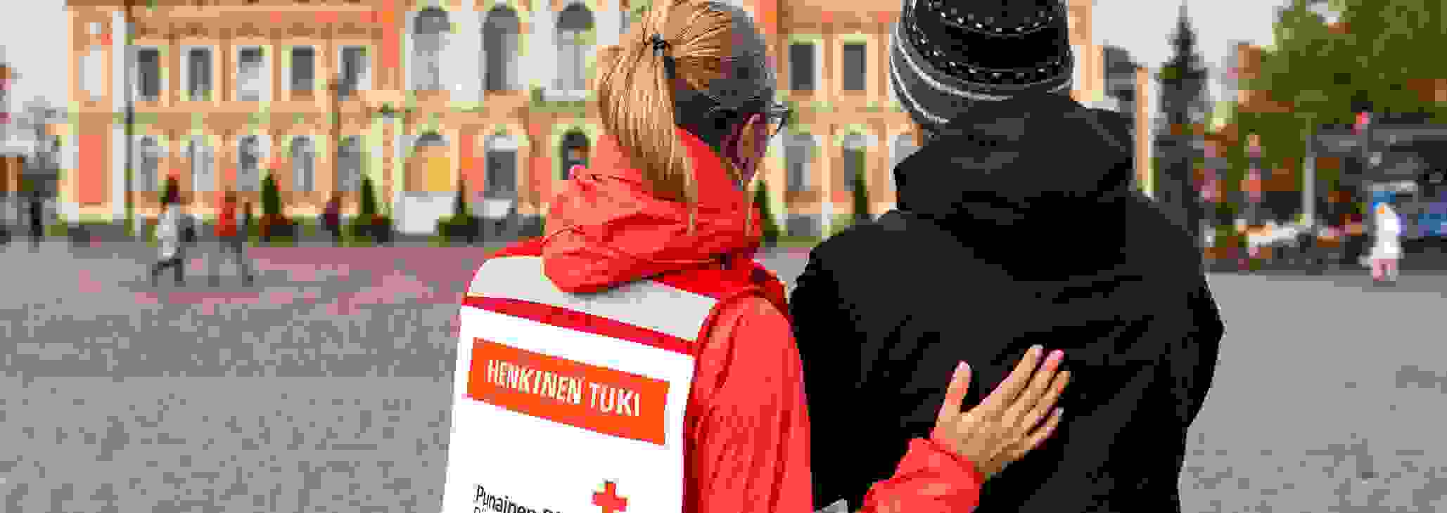Nainen Punaisen Ristin vapaaehtoisliiveissä keskustelee järkyttyneen miehen kanssa Kuopion torilla.