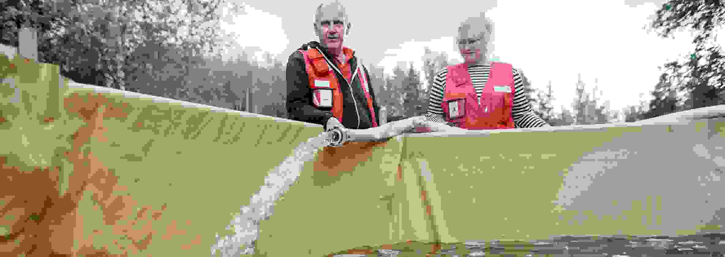 Nainen ja mies Punaisen Ristin varusteissa täyttävät vesiallasta puhtaalla vedellä.