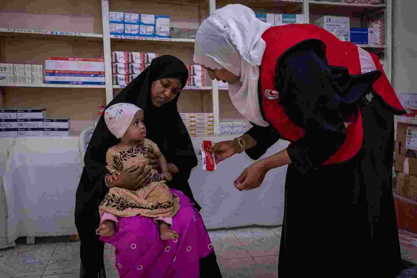 Ett barn och en mamma på en av Röda Halvmånens kliniker. En vårdare ger barnet mat.
