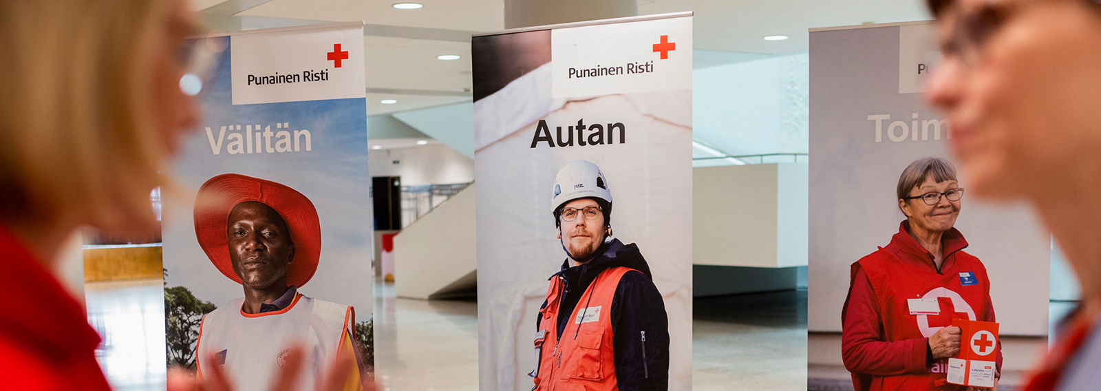 Två personer pratar. I bakgrunden finns tre roll-ups med Röda Korsets volontärer.