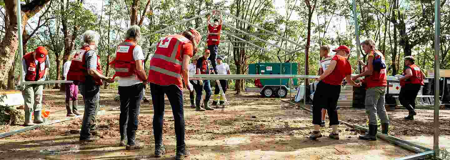 Tretton biståndsarbetare från Röda Korset reser ett sjukhustält på en solig plan i Bangladesh.