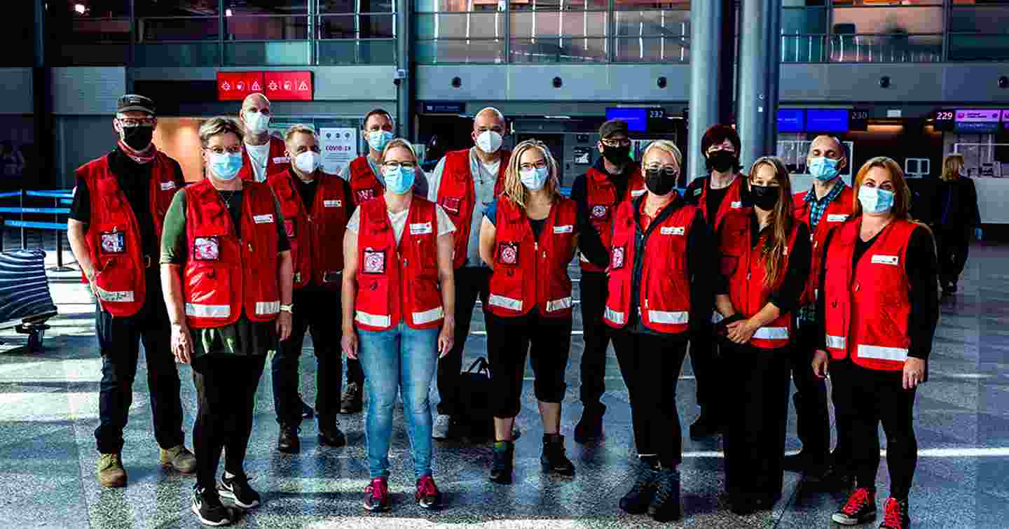 Fjorton biståndsarbetare i Röda Korsets klädsel och munskydd på Helsingfors-Vanda flygplats.