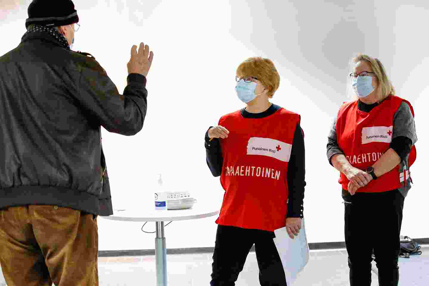 En person på väg till vaccineringen diskuterar med två av Röda Korsets frivilliga.