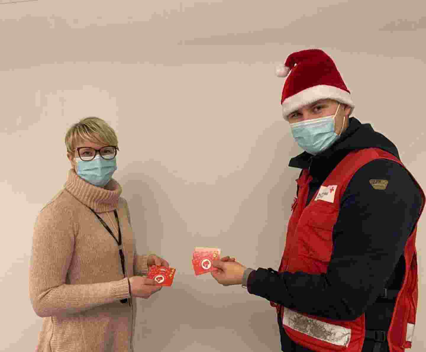 Två personer med munskydd håller matpresentkort i sina händer. Den ena är klädd i Röda Korsets väst och tomteluva.