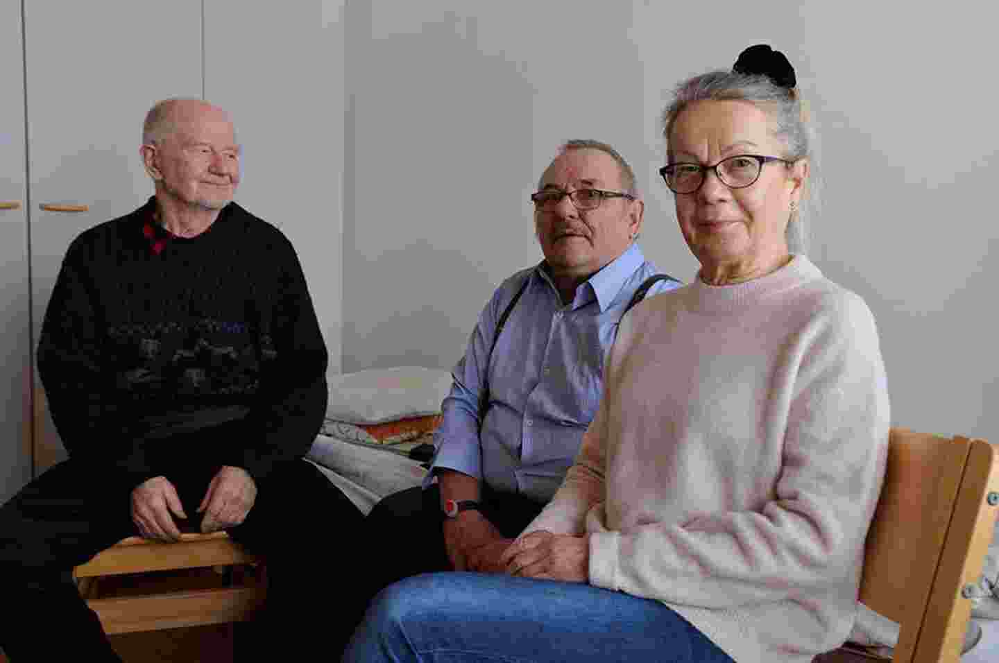 Tre äldre leende personer sitter bredvid varandra.