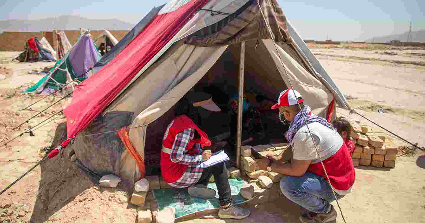 Två arbetare från Röda halvmånen i Afghanistan samtalar med en person som bor i tält.