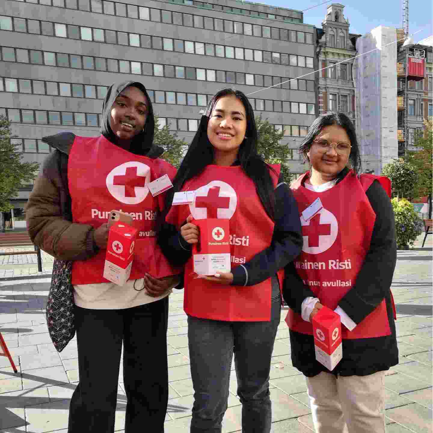 Tre leende ungdomar i Röda Korsets väst och en insamlingsbössa i handen.