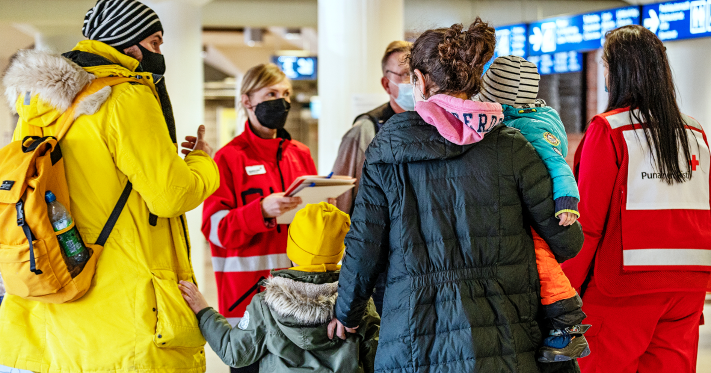 Röda Korsets frivillig diskuterar med en barnfamilj. Alla har vinterjackor på sig.