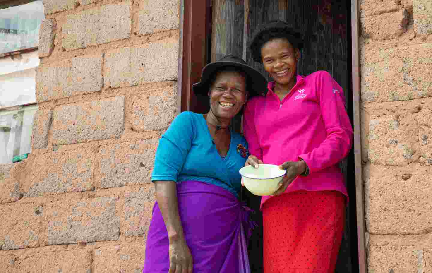 Två leende människor framför sitt bostadshus i Eswatini.