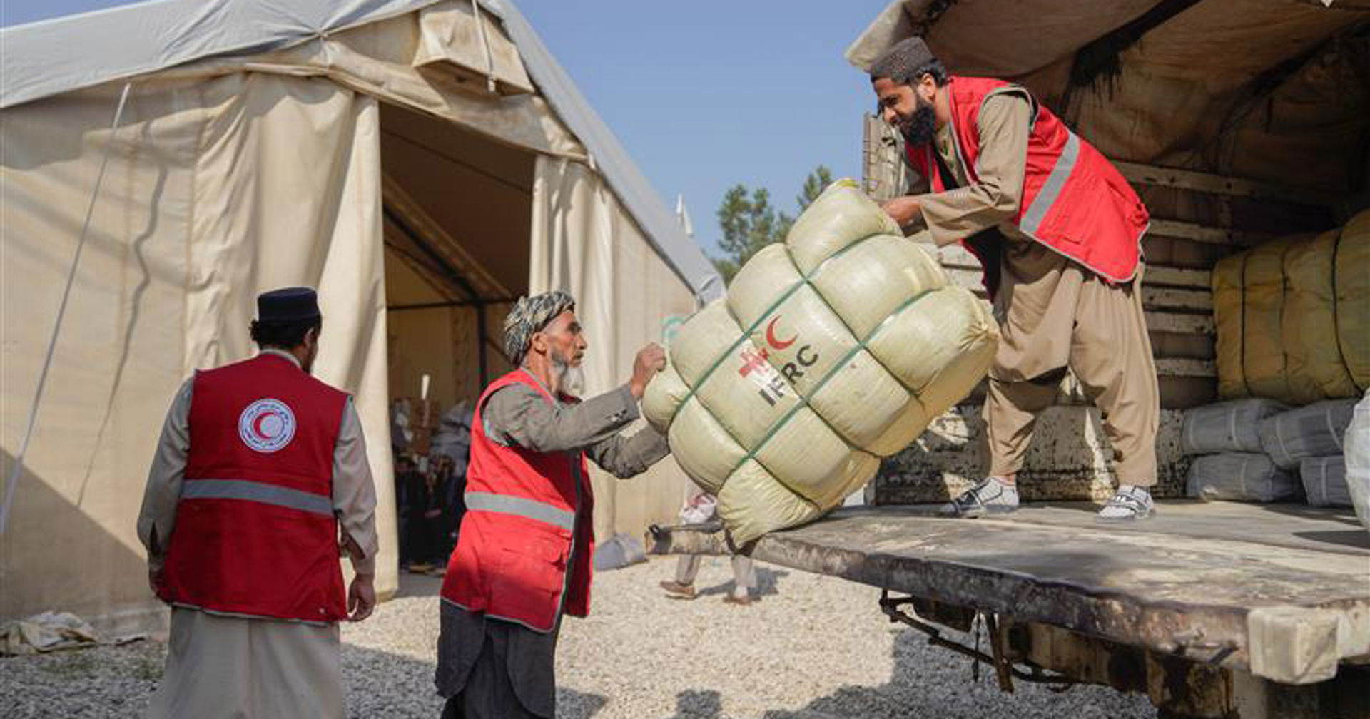 Frivilliga från Afghanska Röda Halvmånen lyfter ett hjälppaket från en lastbil till ett tält i ett katastrofområde.
