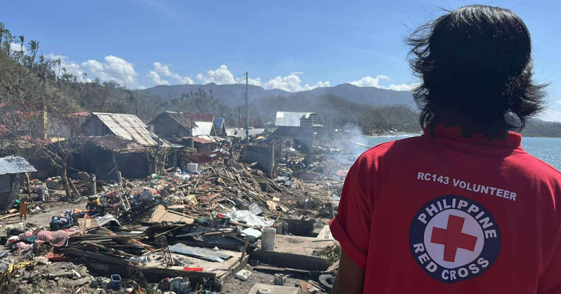 En frivillig från Filippinernas Röda Kors ser ut över ett kustlandskap som är fullt av stormskador, såsom förstörda hus.