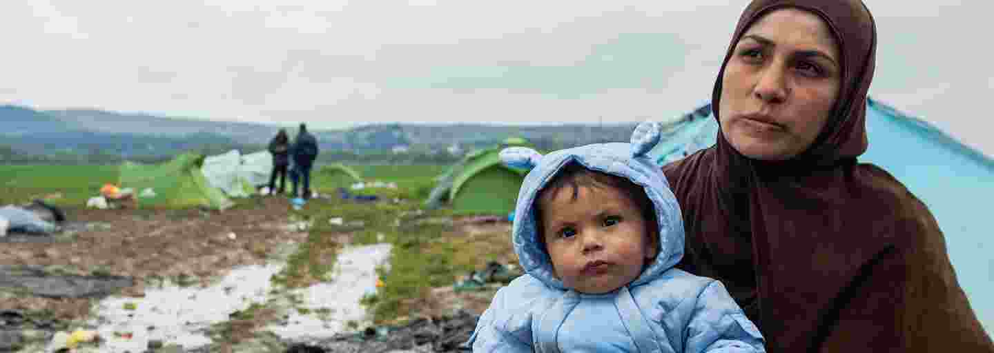 En mamma håller ett spädbarn med varma kläder i sin famn i ett flyktingläger.