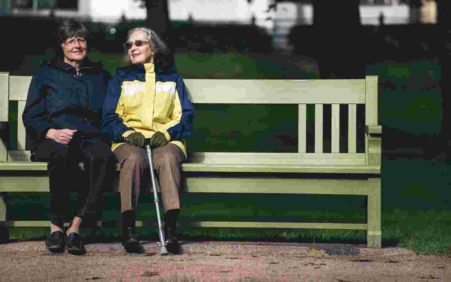 Två äldre kvinnor sitter bredvid varandra på en parkbänk.