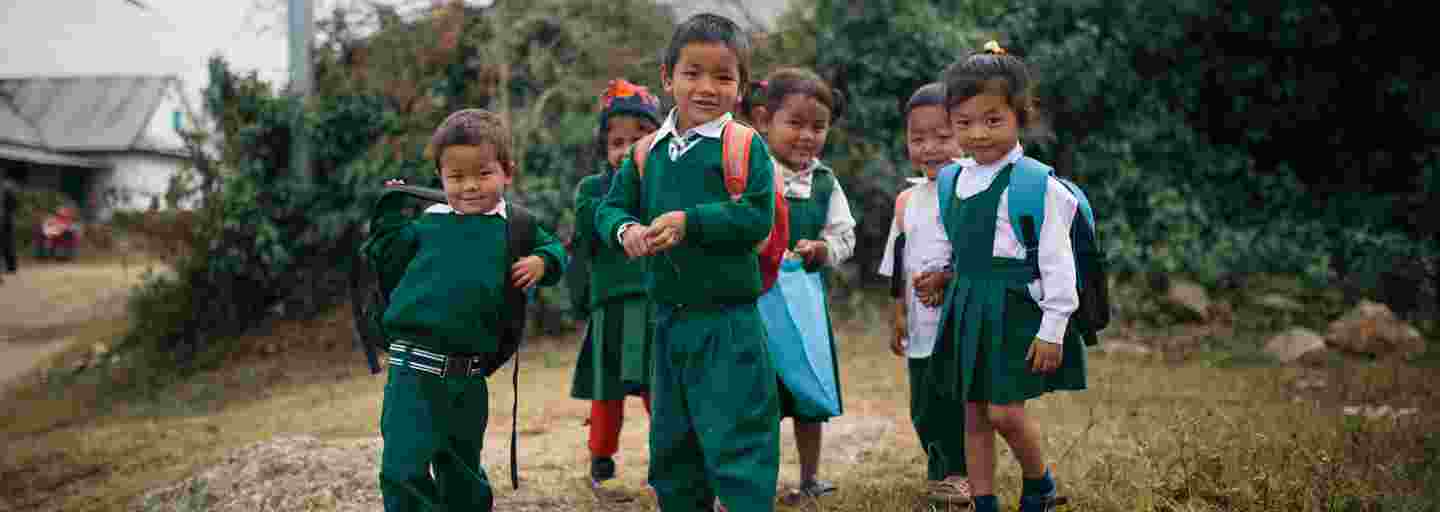 Leende nepalesiska barn i skoluniform på väg till skolan.