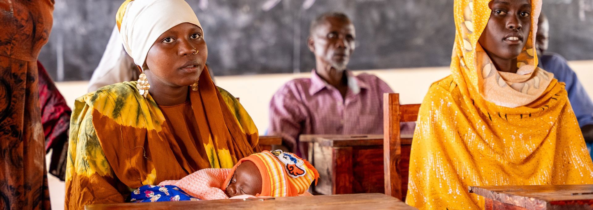 Två av Röda Korsets frivilliga i röda insamlingsvästar håller i insamlingsbössor. Bredvid dem finns en ungefär två meter hög insamlingsbössa.