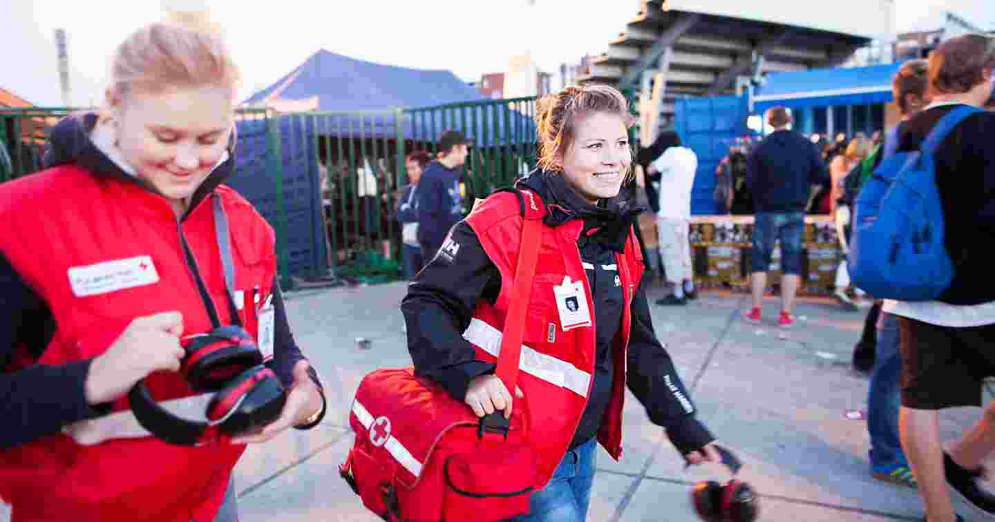 Leende frivilliga första hjälpen-jourhavande från Röda Korset går runt på ett festivalområde.