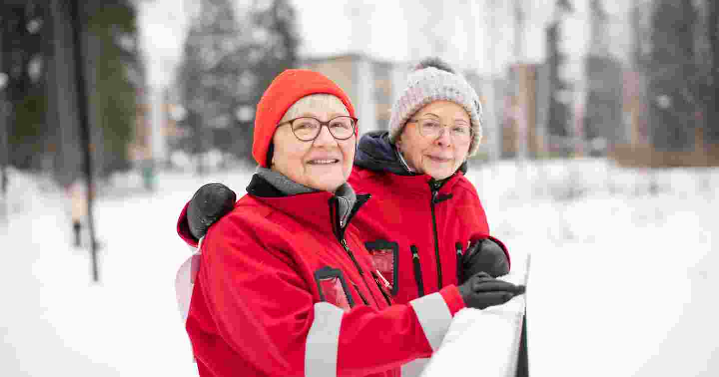 Röda Korsets Tuuli Sundell och Leena Valtee-Kuuskoski står leende bredvid varandra i ett vintrigt landskap.