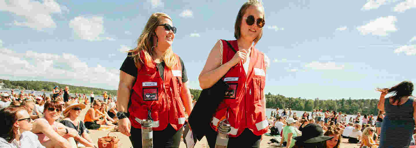 Två unga kvinnor i Röda Korsets västar för frivilliga har första hjälpen-jour på ett soligt Ruisrock.