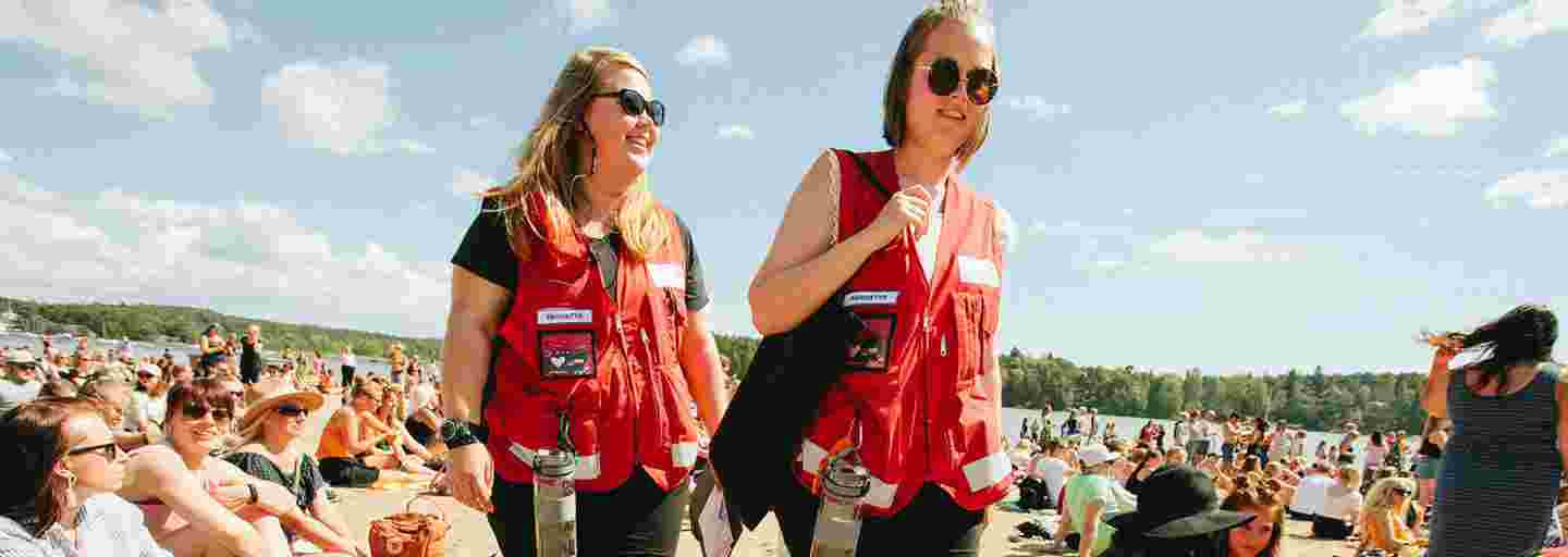 Två unga kvinnor i Röda Korsets västar för frivilliga har första hjälpen-jour på ett soligt Ruisrock.