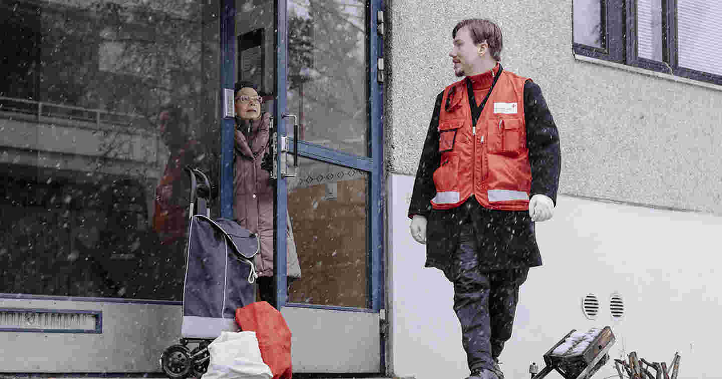 En ung man i Röda Korsets väst för frivilliga hjälper en äldre att handla under coronaepidemin.