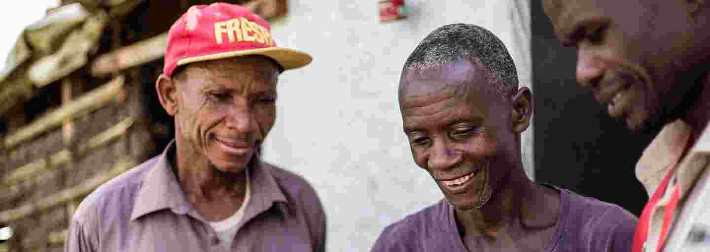 Kolme hymyilevää afrikkalaismiestä tutkii dokumenttia, jossa on tietoa kadonneesta omaisesta.