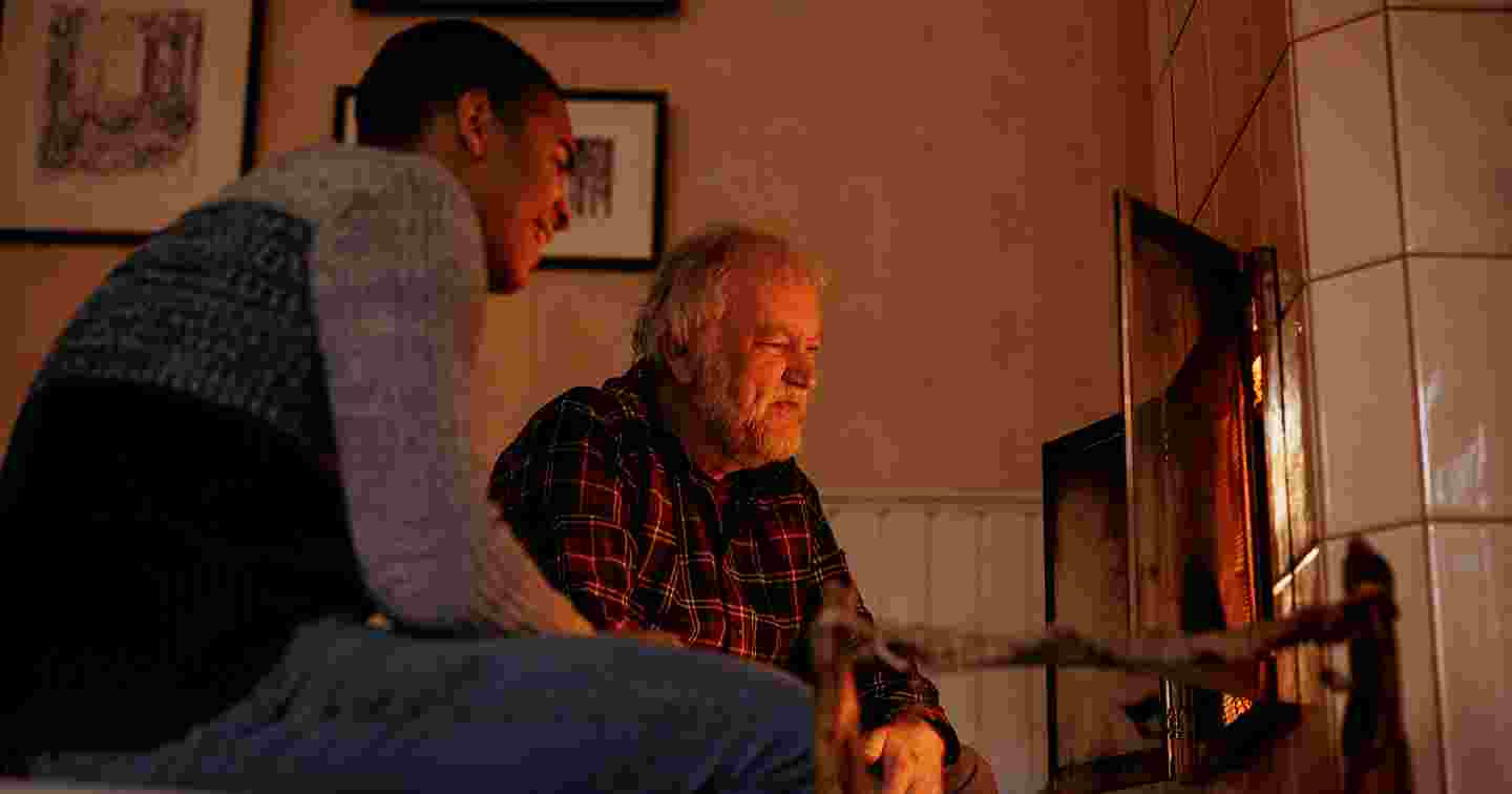 Två äldre personer pratar med varandra med en laptop och smarttelefon i händerna.