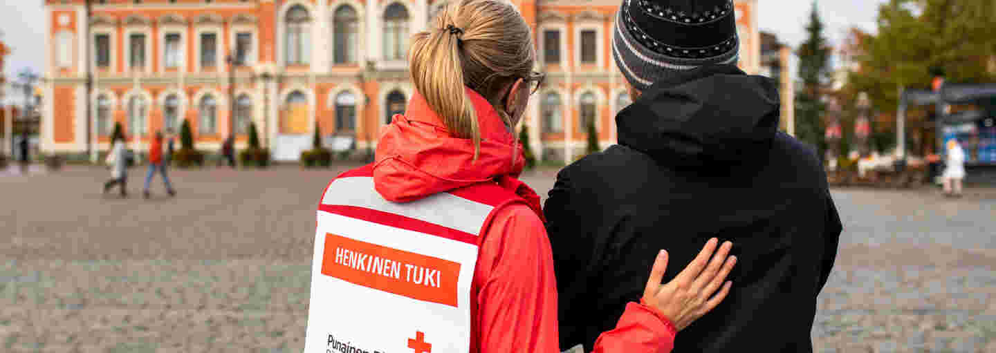 Nainen Punaisen Ristin vapaaehtoisliiveissä keskustelee järkyttyneen miehen kanssa Kuopion torilla.