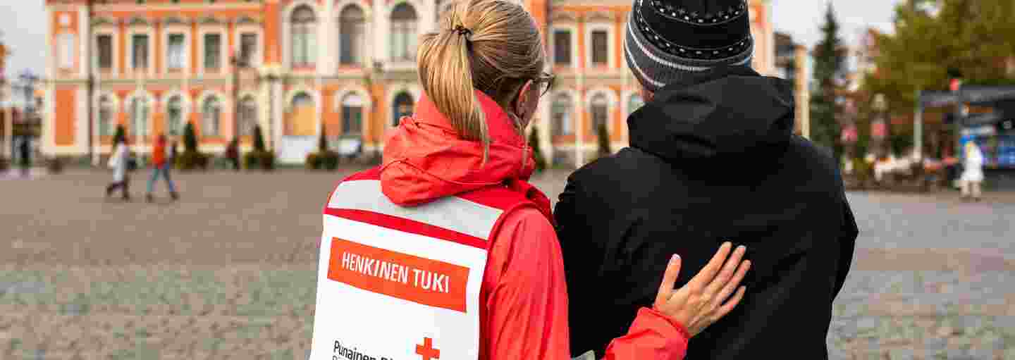 Nainen Punaisen Ristin vapaaehtoisliiveissä keskustelee järkyttyneen miehen kanssa Kuopion torilla.