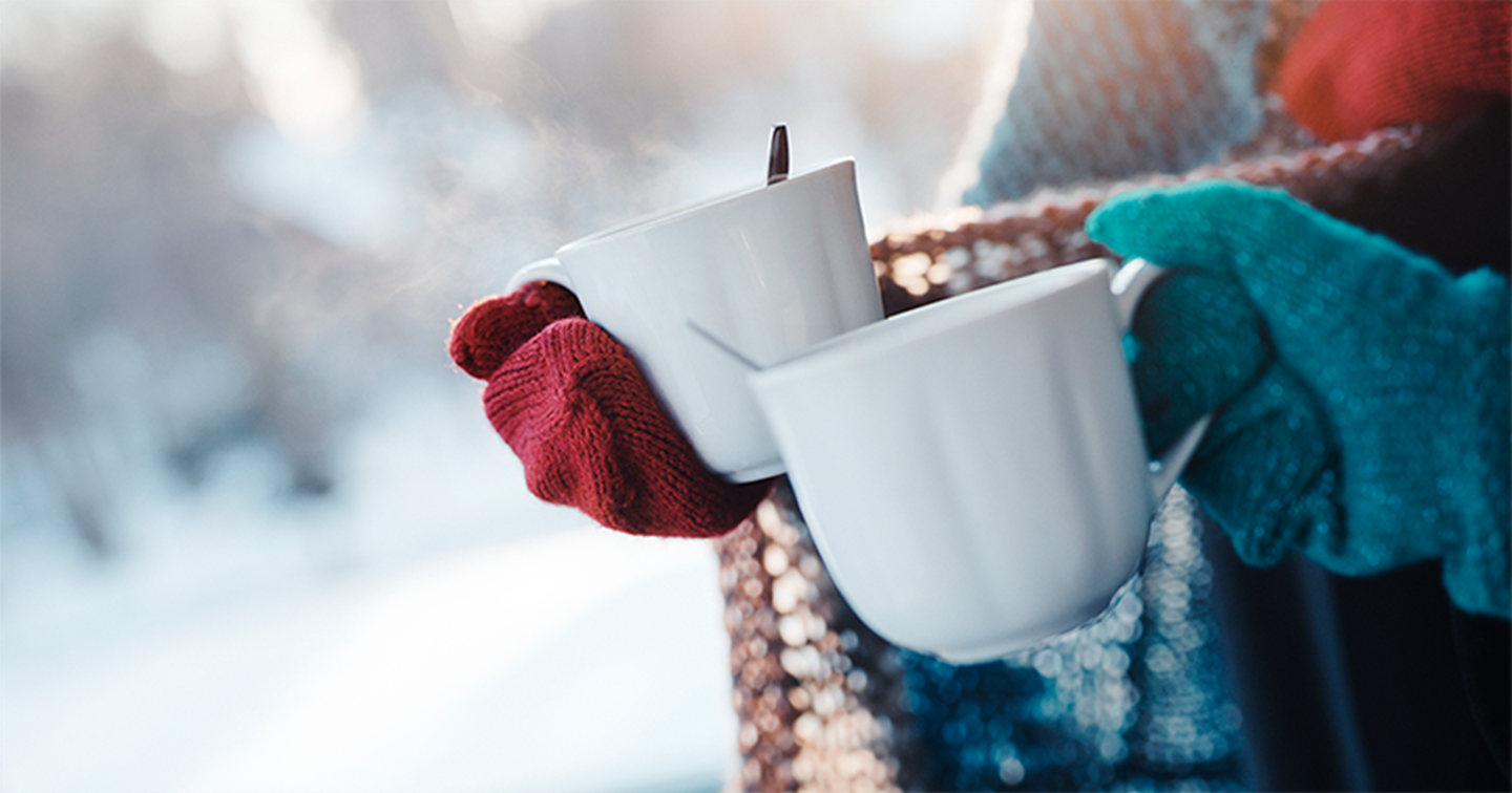 Två personer med en kopp ångande dryck i handen utomhus i vinterväder.