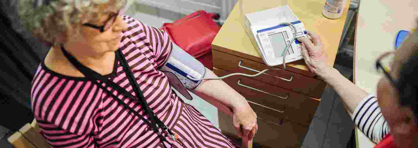 Nainen Punaisen Ristin vapaaehtoisliiveissä mittaa verenpainetta iäkkäältä naiselta.