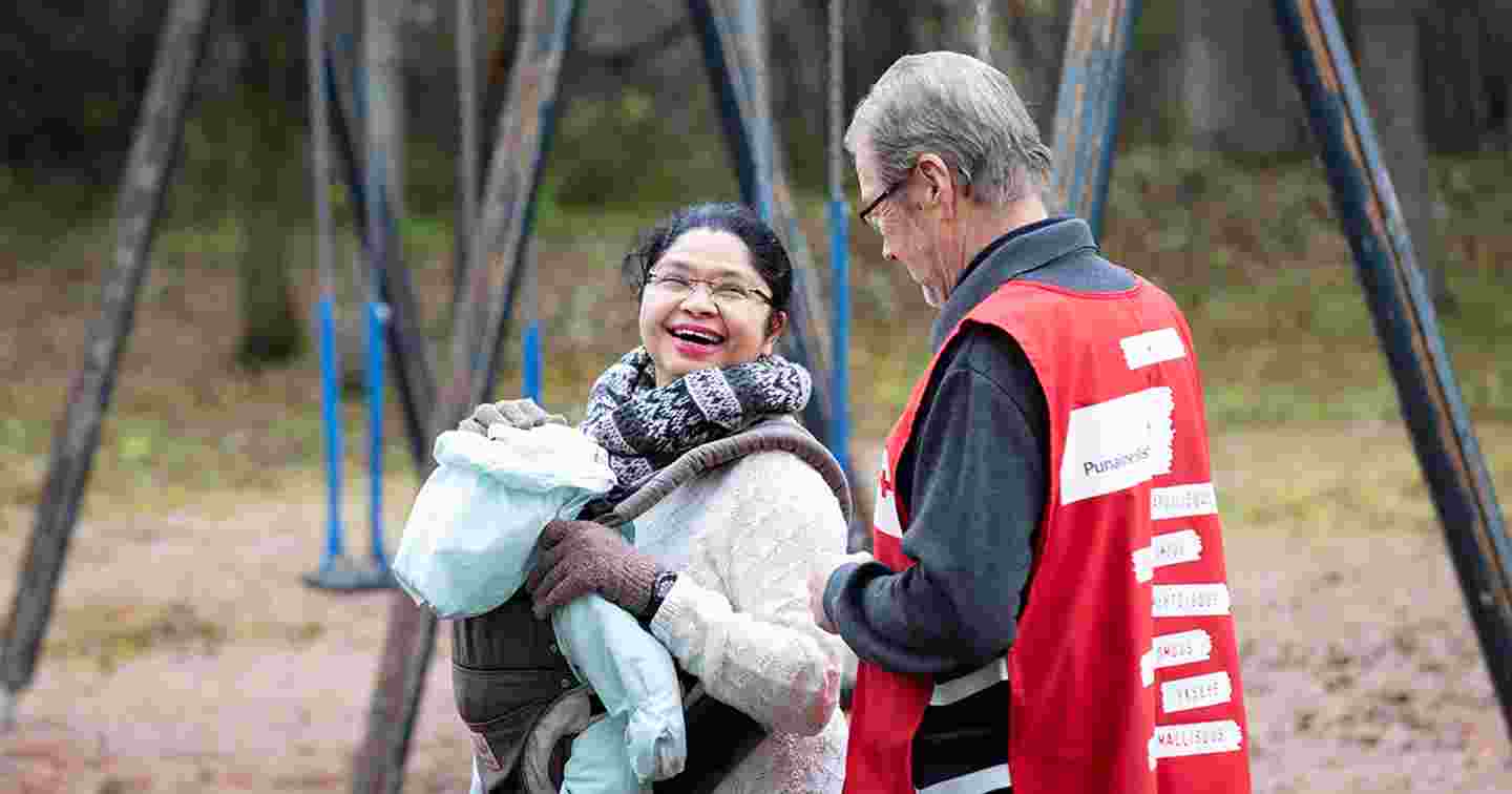 En kvinna i Röda Korsets frivilligväst lär en äldre invandrarkvinna och ett invandrarbarn. Den äldre kvinnan kramar den frivilliga.