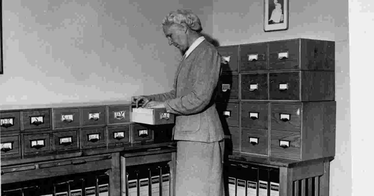 Ett gammalt svartvitt foto av en person som arbetar med ett kartotek över sjukskötare.