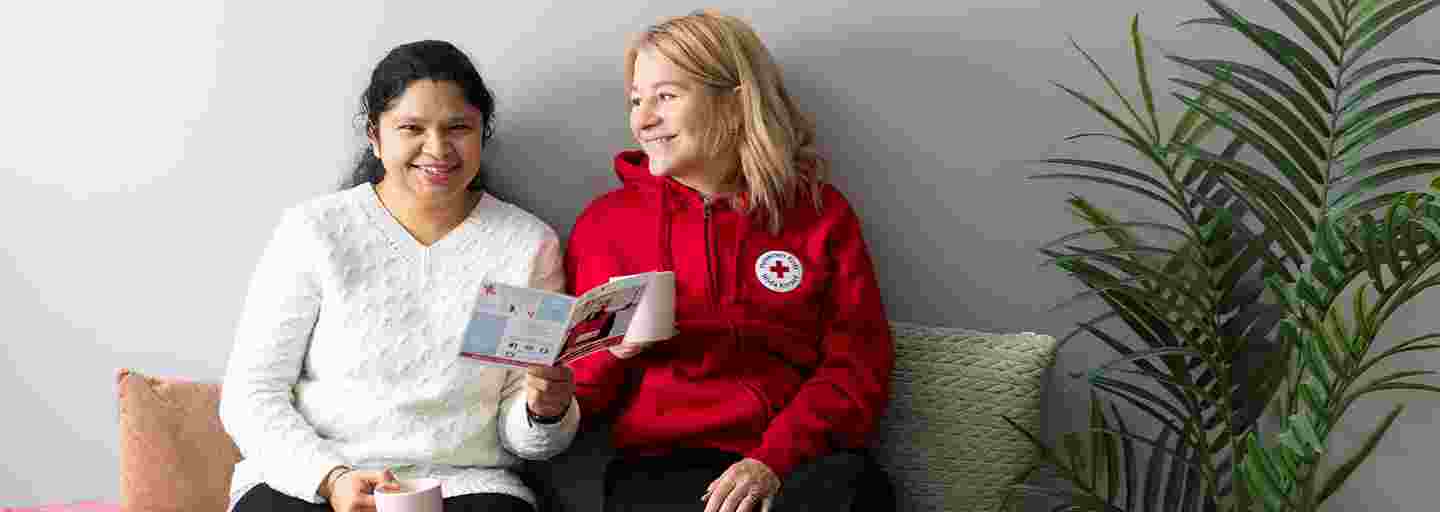 Två leende personer sitter på en soffa och läser Röda Korsets broschyr.