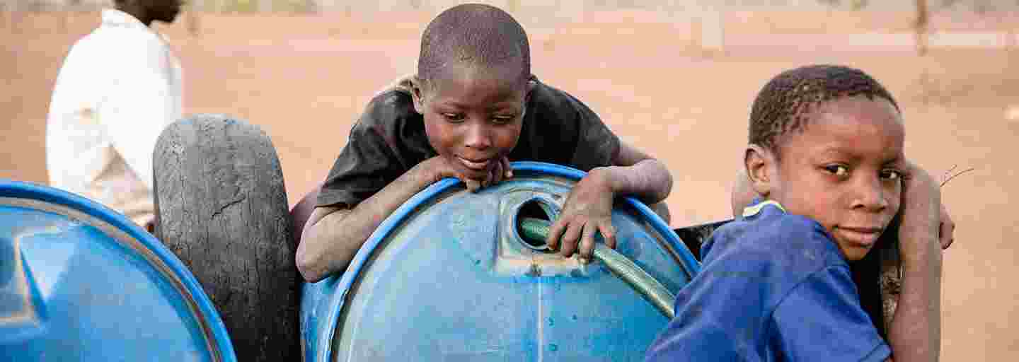 Tre zimbabwiska pojkar bredvid behållare med rent vatten.