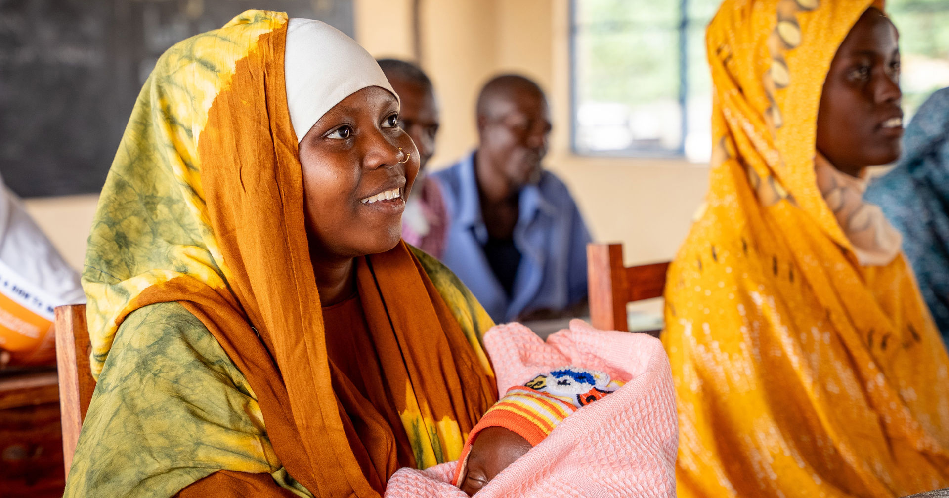 En bonde som är iklädd arbetsoverall ler med en flåhacka i handen.