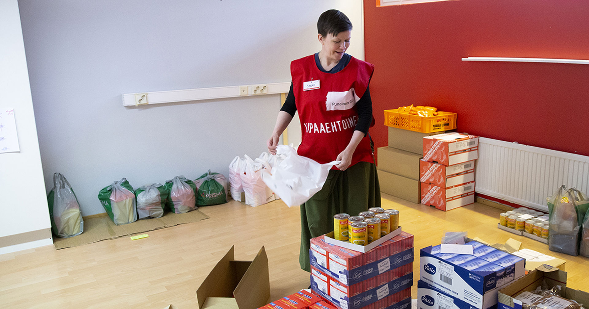 En person i Röda Korsets väst för frivilliga packar livsmedel med ett leende på läpparna.