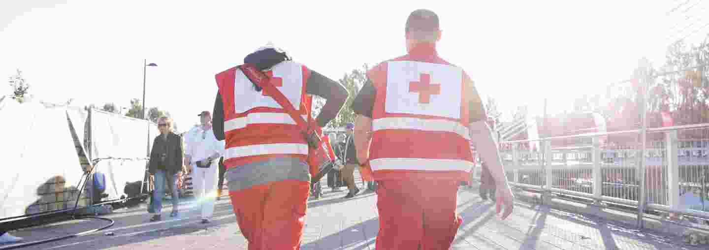 En man och en kvinna som har på sig Röda Korsets utstyrslar och som dejourerar för första hjälpen i ett utomhusevenemang går mot solnedgången.