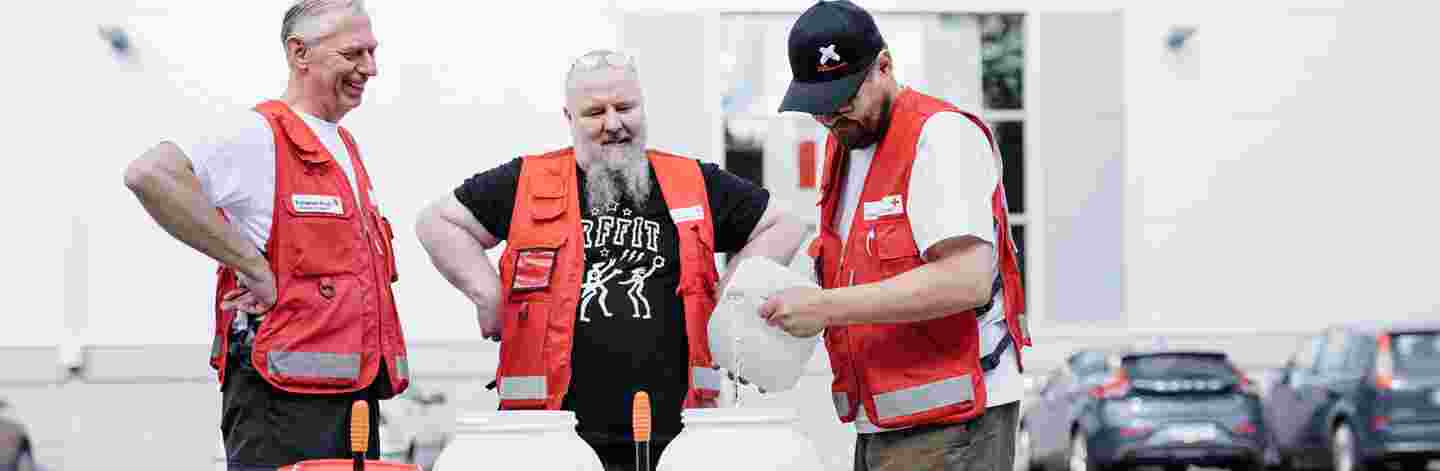 Tre leende män i Röda Korsets kläder fyller på behållare med rent vatten.