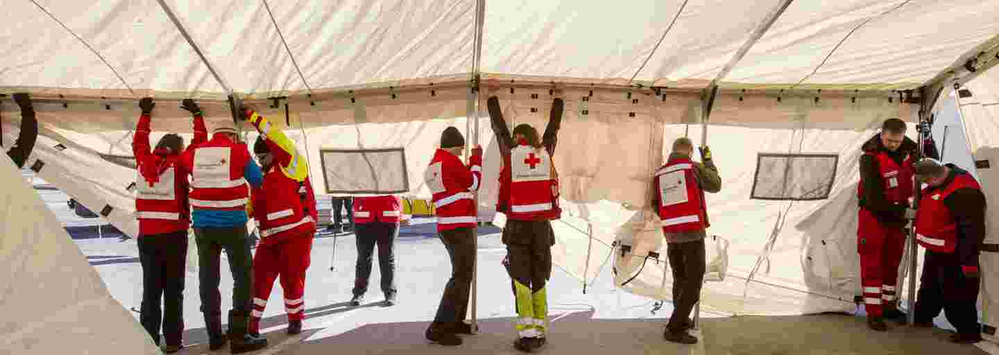 Sju personer klädda i Röda Korsets kläder reser ett tält.