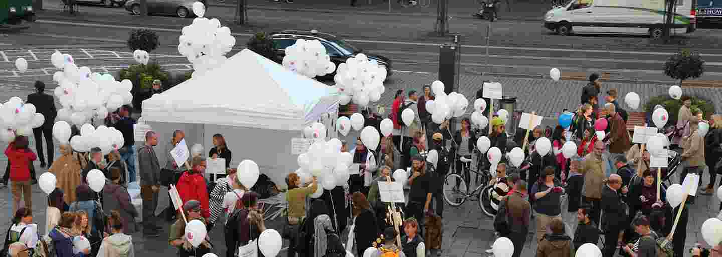 Tiotals människor med ballonger i händerna på ett torg under ett evenemang mot rasism.