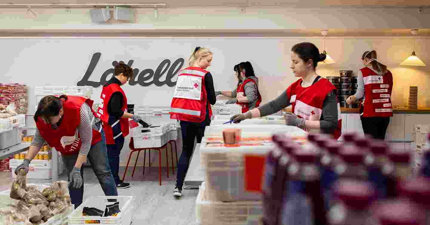 Sex personer i Röda Korsets frivilligvästar organiserar matförpackningar.