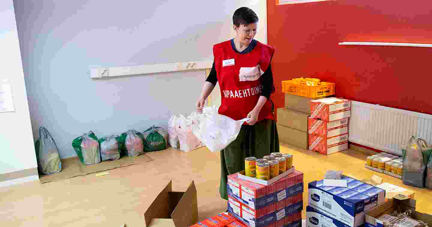 En person i Röda Korsets väst för frivilliga packar livsmedel med ett leende på läpparna.
