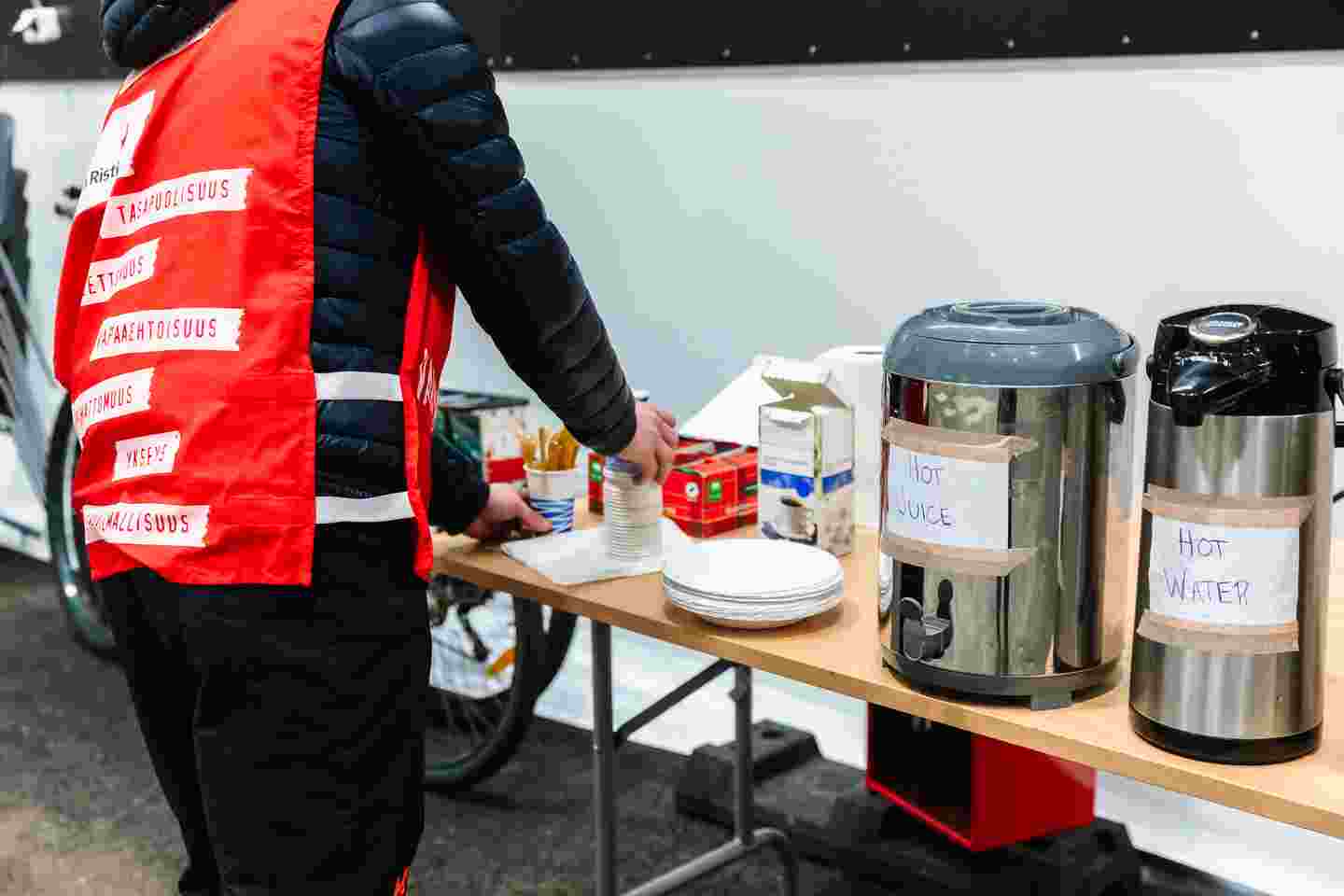 En frivillig från Röda Korset ordnar ett bord med varma drycker i termoskärl.