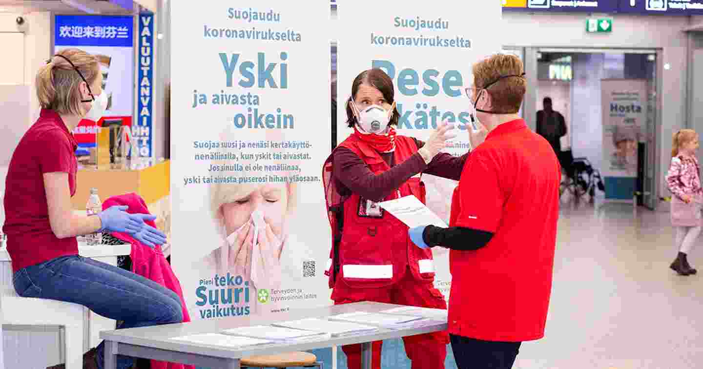 Tre personer i Röda Korsets västar vid en coronarådgivningspunkt på Helsingfors–Vanda flygplats.