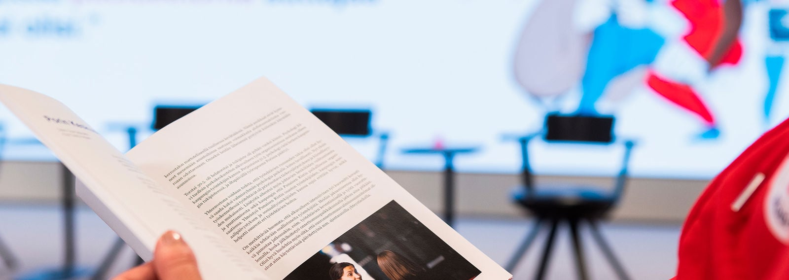 En person klädd i Röda Korsets huvtröja bläddrar i en broschyr i handen.